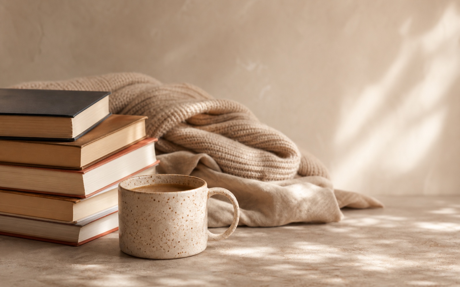 A stack of books, ceramic coffee mug, and warm linen in soft natural light